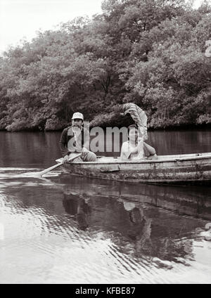 PANAMA, Panama Canal Zone, Barro Colorado, a man paddles a boat and a woman shades herself with a large leaf, Central America Stock Photo