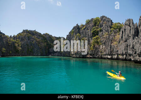 PHILIPPINES, Palawan, El Nido, Miniloc Island, a woman kayaks through the crystal clear waters of Small Lagoon on Miniloc Island located in Bacuit Bay Stock Photo