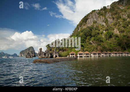 PHILIPPINES, Palawan, El Nido, Lagen Island, view of surrounding rock formations, a fishing boat and Lagen Island Resort cottages in Bacuit Bay in the Stock Photo