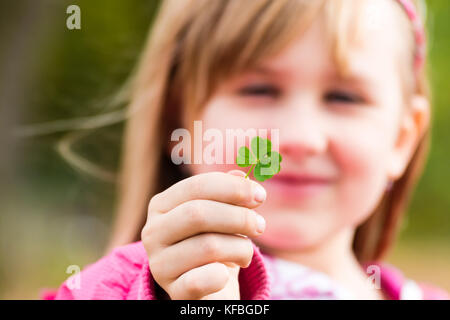 Four leaf clover in small hand of young girl in front of her face. Girl's face on background. Selective focus. Stock Photo