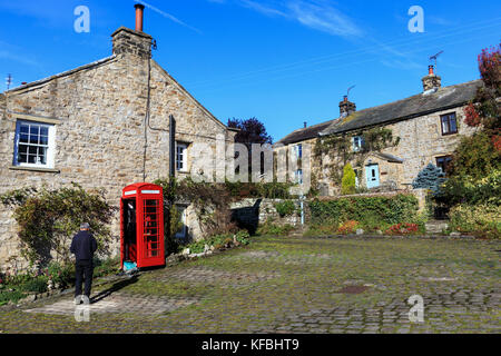 Stone built houses in the village of Healaugh Richmond a man by a traditional red British Telephone box NorthYorkshire England Stock Photo
