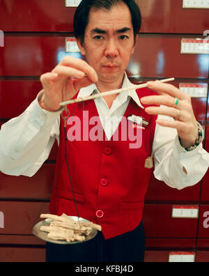 SINGAPORE, Asia, portrait of a Chinese man weighing herbal medicine at the Eu Yan Sang Shop. Stock Photo