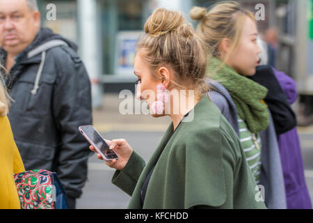 Young woman in a busy city walking while looking down at a smartphone in Brighton, East Sussex, England, UK. Stock Photo