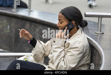 Young woman using the phone while smoking a cigarette in the UK. Stock Photo