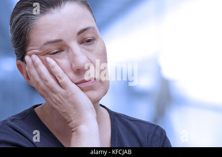 Middle aged woman nearly falling asleep in the office. Tiredness because of sleep apnea syndrome, insomnia or fibromyalgia, blue filter effect Stock Photo
