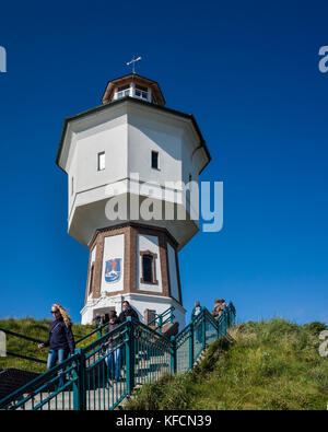 Wasserturm Langeoog. Germany Deutschland.  Holiday makers walking down the steps as the leave the water tower, which is one of Langeoog's main tourist attractions.  It's a sunny day making a nice blue sky to contrast the white of the water tower.  Previous visitors have left padlocks locked to the railings, which can be seen in the foreground.  Photographed with a Ricoh GRII camera. Stock Photo