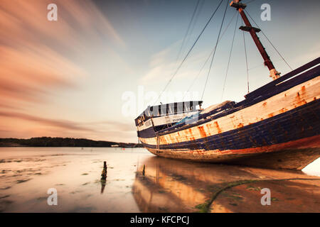 Long exposure image of an aging corroded traditional commercial boat. Dramatic sky enhances this wooden ship with reflection on water in Bali, Indo Stock Photo