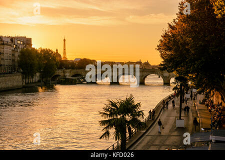 Late summer sunset on Paris with the Eiffel tower and the 'Pont Neuf' bridge in the background and people strolling on the wharf of the river Seine in Stock Photo