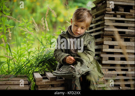 A small sad boy dressed in a military dress is resting after a trip Stock Photo