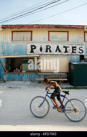 BELIZE, Caye Caulker, a boy rides his bike past pirates restaurant Stock Photo