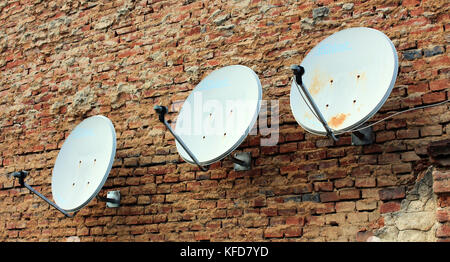 Three white satellite dishes mounted on old brick wall Stock Photo