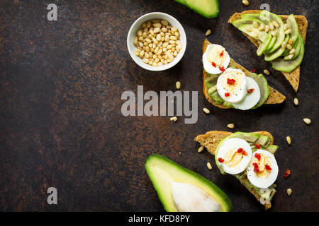 Sandwich avocado with fresh sliced avocado, egg poached and spices on a dark slate or stone background. Copy space. Flat lay, top view. Stock Photo