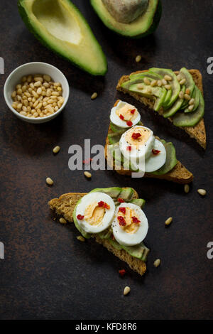 Sandwich avocado with fresh sliced avocado, egg poached and spices on a dark slate or stone background. Copy space. Flat lay, top view. Stock Photo