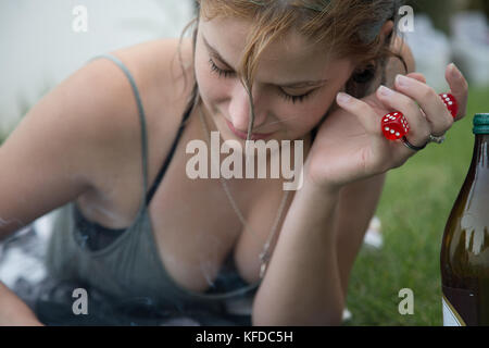 Young woman lying on garden grass having beer and smoking cigarette looking at camera. Stock Photo