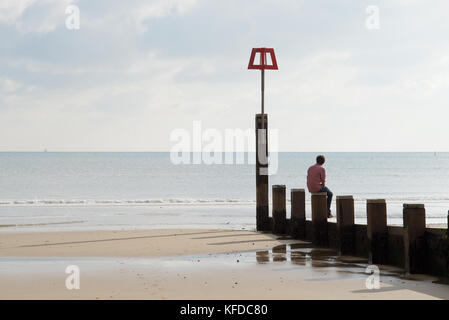 Young man sitting on a groyne looking out to sea Stock Photo