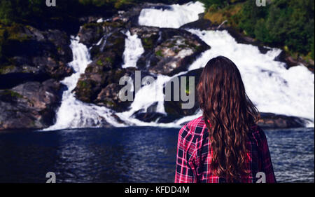 Young woman with long hair and red shirt looking at Hellesyltfossen, a waterfall in Hellesylt, Norway Stock Photo