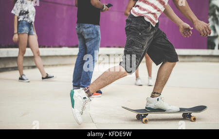 Close up of a group of people standing in a skate park and riding a skateboard. Stock Photo