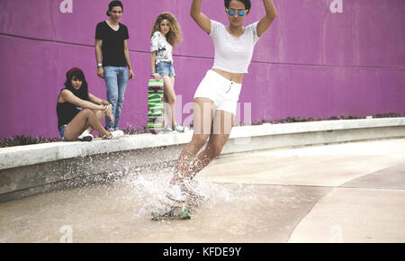 A young woman riding a skateboard through water. Stock Photo