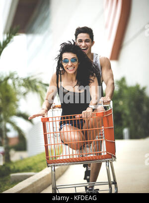 A young man pushing a young woman sitting in a shopping trolley. Stock Photo