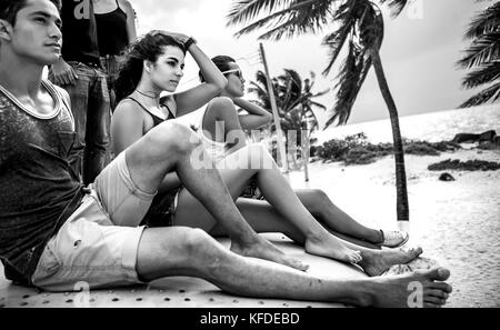 Young people sitting on a beach and looking out to sea. Stock Photo
