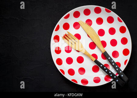 table setting with a bamboo knife, fork and plate with polka dots on a dark background Stock Photo