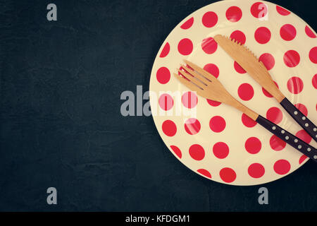 Retro table setting with a bamboo knife, fork and plate with polka dots on a dark background Stock Photo