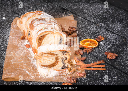 Appetizing looking sponge cake, homemade, sliced and displayed on the baking paper, filled with poppy seeds and walnuts, covered with powder sugar. Stock Photo