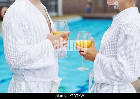 Romantic couple in white bathrobes standing by swimming-pool with drinks Stock Photo