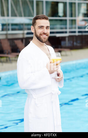 Happy man in white bathrobe standing by swimming-pool of his hotel Stock Photo