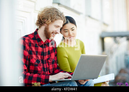 Two modern students with laptop working over college project outdoors Stock Photo