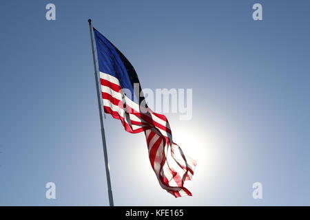 The American Flag flying proud against the sun in a clear blue sky.