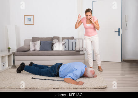 Shocked Young Woman Looking At Her Fainted Disabled Father Lying On Carpet Stock Photo