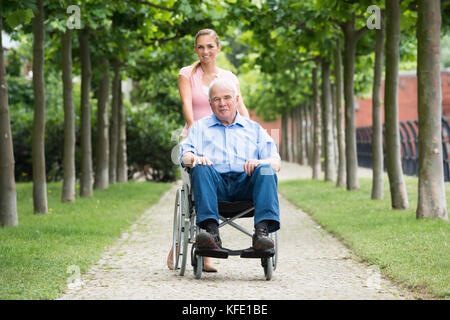 Happy Young Woman With Her Old Senior Father On Wheelchair In Park Stock Photo