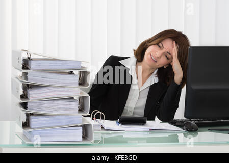 Stressed Young Businesswoman Looking At Stack Of Folders In Office Stock Photo