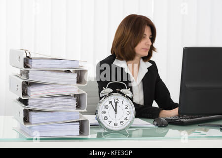 Businesswoman Working On Computer In Office With Alarm Clock On Desk Stock Photo