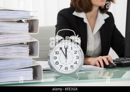 Close-up Of Young Businesswoman Working On Computer In Office With Alarm Clock On Desk Stock Photo