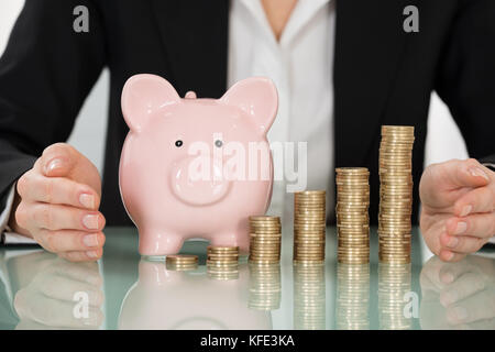 Close-up Of Businesswoman Protecting Coins And Piggybank On Desk Stock Photo