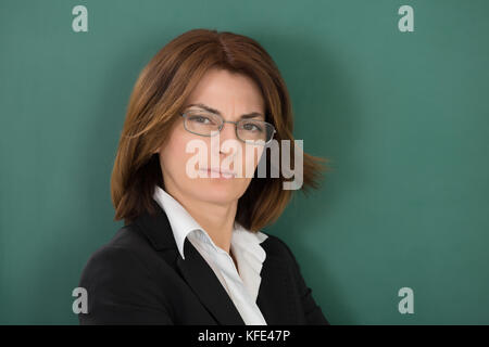 Portrait Of Young Female Teacher Standing Against Green Chalkboard Stock Photo