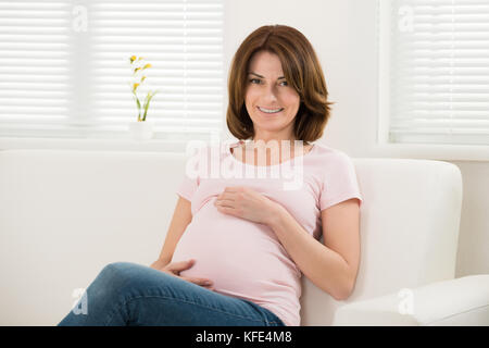 Happy Young Pregnant Woman Sitting On Sofa Stock Photo