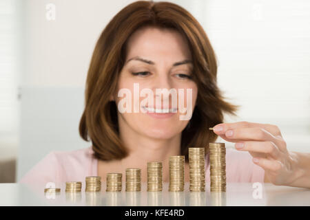 Young Happy Woman Stacking Coins At Desk Stock Photo