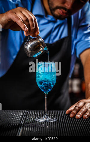 Barman is adding some blue liquid in a glass, he is preparing blue lagoon cocktail Stock Photo