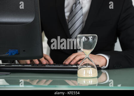 Businessman Working On Computer With Hourglass On Desk Stock Photo