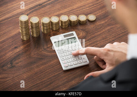 Close-up Of Businessman Calculating With Calculator In Front Of Stacked Coins At Desk Stock Photo