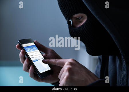 Close-up Of Hacker Using Smart Phone To Steal Data In Office Stock Photo