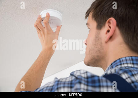 Male Electrician With Screwdriver Repairing Fire Sensor Stock Photo