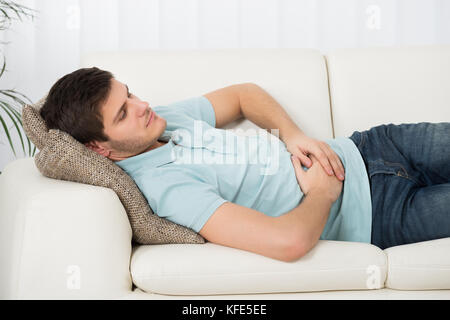 Man Suffering From Stomach Ache Lying On Sofa Stock Photo