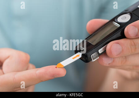 Close-up Of Young Man Hand Using Glucometer To Check Blood Sugar Level Stock Photo