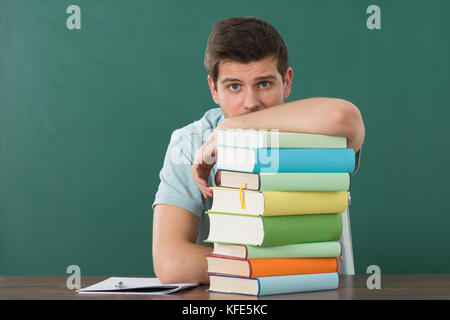 Young Man Leaning On Stack Of Books At Desk Stock Photo