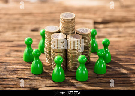 Stack Of Coins Surrounded With Green Figures On Wooden Desk Stock Photo