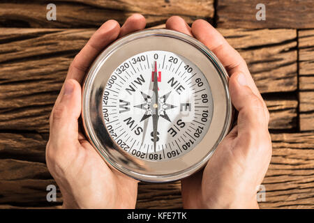 Close-up Of A Hands Holding Magnetic Compass Over The Wooden Desk Stock Photo